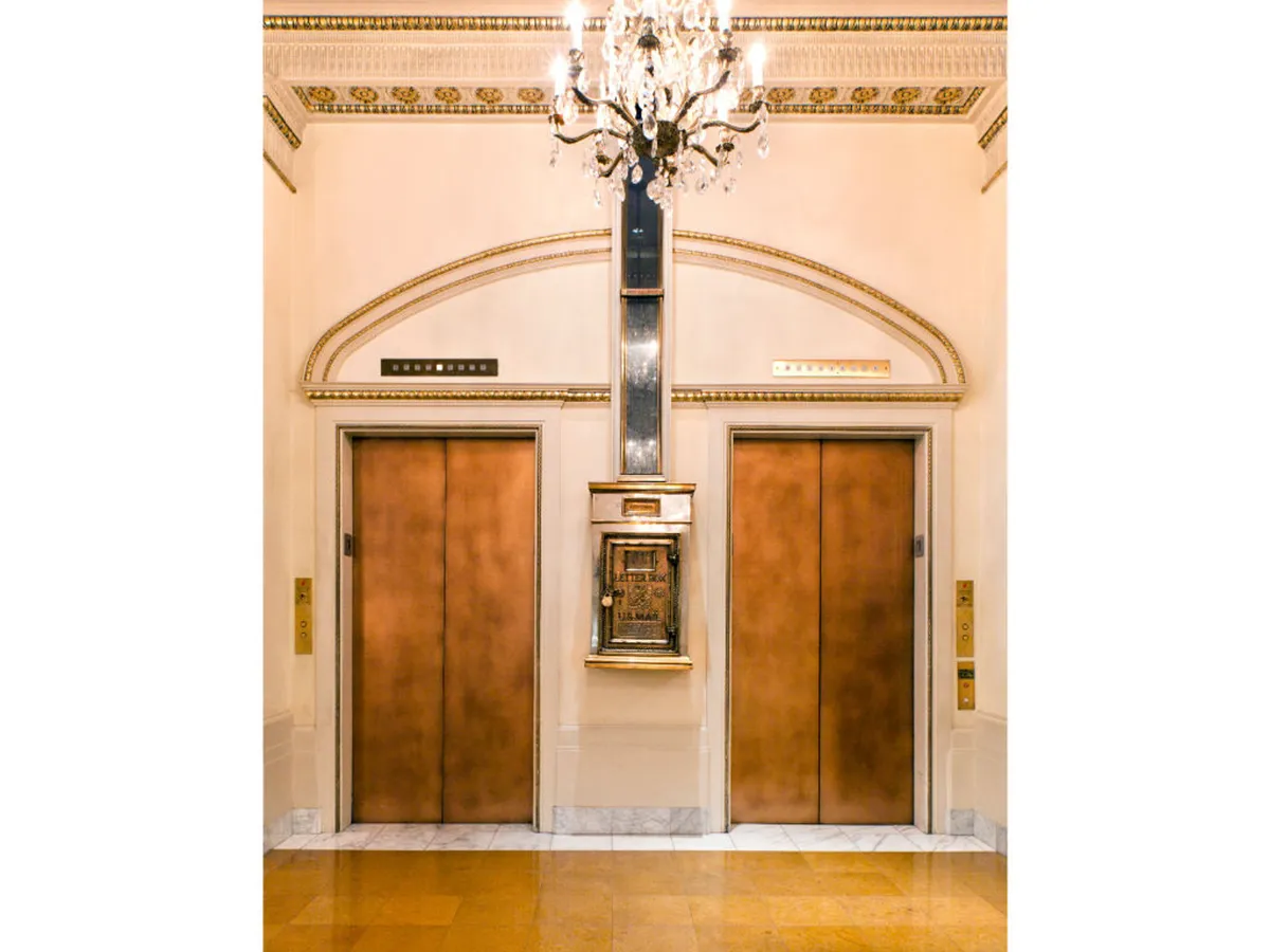 A sophisticated elevator lobby interior with ornate detailing, a chandelier, and elevator call buttons, suggesting refined, modern amenities and ease of access throughout the hotel.