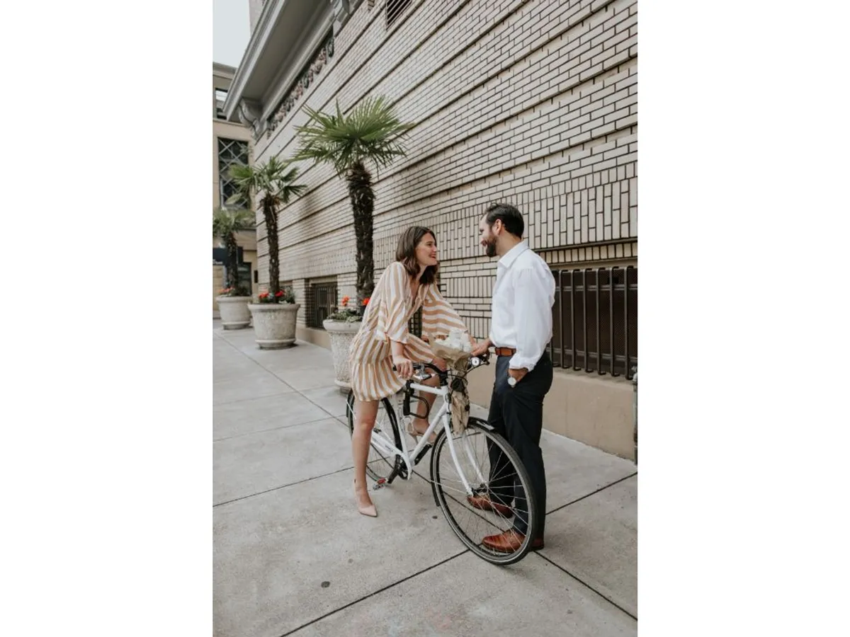 This exterior image features a couple with a bicycle amidst palm trees, evoking a sense of playful adventure and healthy activity. The setting suggests urban exploration and the joy of cycling together, set against a backdrop of city greenery.