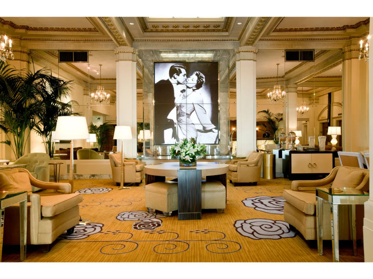 A stylish guest room lounge with luxurious seating, a striking black-and-white artwork of a couple kissing, and a central floral arrangement, all exuding romance and timeless elegance.