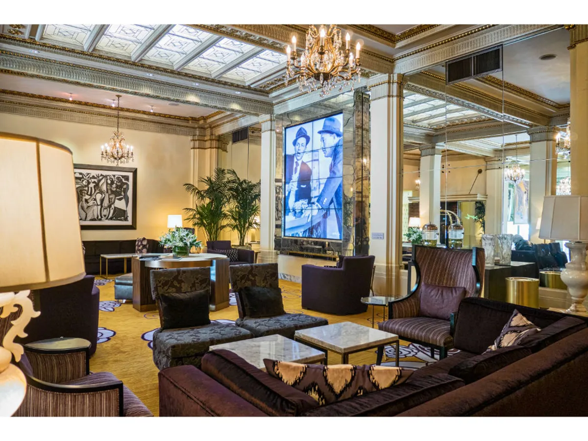 A sophisticated lounge with a statement chandelier, large artwork on the wall, modern TV display, lush green plants, and luxurious seating. The setting is lively yet intimate—perfect for cocktails, art appreciation, and relaxed socializing.